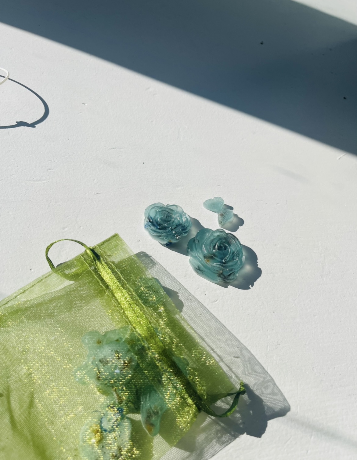 Tiny blue rose-shaped soaps next to a green organza gift pouch